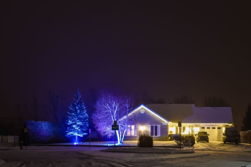 Snow-covered ranch with warm white roofline lights and trees wrapped in holiday lights